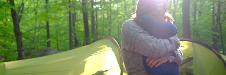 Woman hugging her camping pillow nearby her tent in the forest