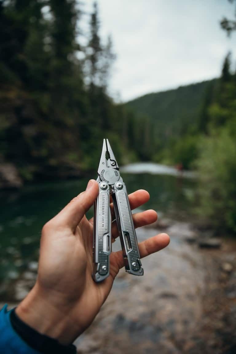 Hand holding a backpacking multitool with path in the forest in the background