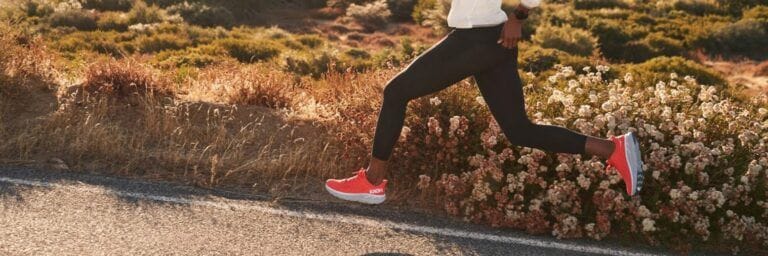 close up on a woman's legs running with orange hoka clifton running shoes